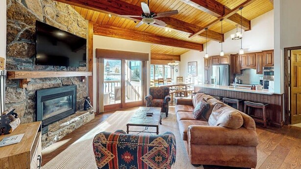 A spacious living area with a stone fireplace, a large TV, and a ceiling fan. - Luxury condo next to lift with pool, hot tubs & high-speed WiFi (Steamboat Springs)
