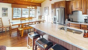 A kitchen with wooden cabinets, a stainless steel refrigerator, a marble island, and a dining area with wooden chairs and a table. - Luxury condo next to lift with pool, hot tubs & high-speed WiFi (Steamboat Springs)