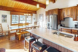 A kitchen with wooden cabinets, a stainless steel refrigerator, a marble island, and a dining area with wooden chairs and a table. - Luxury condo next to lift with pool, hot tubs & high-speed WiFi (Steamboat Springs)