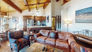 A spacious living area with a wooden ceiling, a sofa, a patterned armchair, a coffee table, and a dining area with a wooden table and chairs. - Luxury condo next to lift with pool, hot tubs & high-speed WiFi (Steamboat Springs)