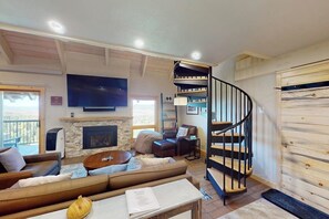 Ein Wohnzimmer mit einer Couch, einem Couchtisch, einem Kamin, einem Fernseher und einer Wendeltreppe.