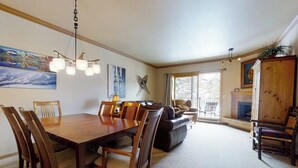 A dining area with a wooden table and chairs, a chandelier, and artwork on the walls. - Charming condo just steps to base area w/shared pool, hot tub, free WiFi (Steamboat Springs)