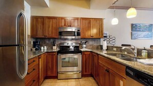 A kitchen with wooden cabinets, stainless steel appliances, a granite countertop, and a built-in dishwasher. - Charming condo just steps to base area w/shared pool, hot tub, free WiFi (Steamboat Springs)