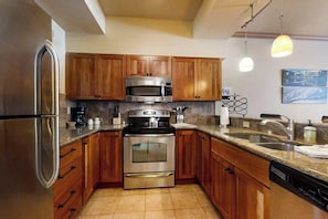A kitchen with wooden cabinets, stainless steel appliances, a granite countertop, and a built-in dishwasher. - Charming condo just steps to base area w/shared pool, hot tub, free WiFi (Steamboat Springs)