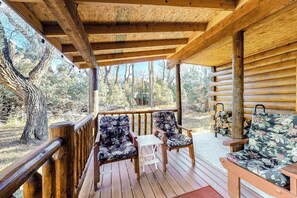 Eine Holzterrasse mit Geländer, zwei stuhlähnliche Sitzgelegenheiten mit Blumenmuster, ein kleiner Tisch und im Hintergrund eine Kabine sowie Bäume.
