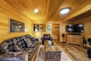 Ein Holzblockhaus-Innenraum mit Sofa, Sessel, Couchtisch, Fernseher und Holzschränken.