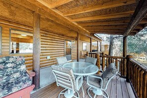 A wooden deck with a round glass table and chairs, a floral sofa, and a wooden railing. - Ideal Gem on the River w/ Wood-Burning Fireplace, Spacious Deck, & WiFi (South Fork)