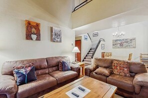 A living room with two brown leather sofas, a wooden coffee table, and a staircase leading to an upper level. - Large & comfy condo with pool, hot tubs, clubhouse & sauna (Steamboat Springs)