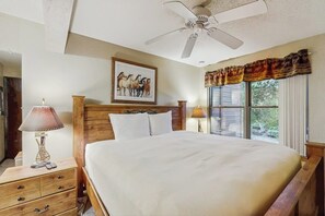 A bedroom with a bed, a nightstand, a lamp, a ceiling fan, a window with curtains, and a framed picture on the wall. - Large & comfy condo with pool, hot tubs, clubhouse & sauna (Steamboat Springs)