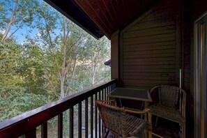 A wooden porch with a table and two wicker chairs, overlooking a forested area. - Large & comfy condo with pool, hot tubs, clubhouse & sauna (Steamboat Springs)