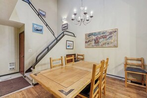 A dining area with a wooden table and chairs, a chandelier, and a staircase. - Large & comfy condo with pool, hot tubs, clubhouse & sauna (Steamboat Springs)