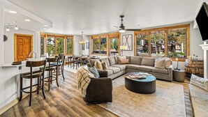 Een ruime woonkamer met een grote hoekbank, een salontafel en een eethoek met barstoelen.