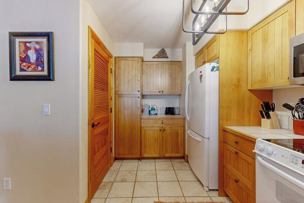 Eine kleine Küche mit Holzschränken, einem Kühlschrank, einer Mikrowelle und einem Herd.