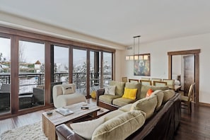 A spacious living room with a large sliding glass door leading to a balcony, a sofa set, a coffee table, and a painting on the wall. - Luxurious corner condo w/ view & shared pool, hot tubs, game room & more (Steamboat Springs)