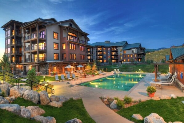 A multi-story hotel with a pool, outdoor seating, and a well-maintained garden. - Luxurious corner condo w/ view & shared pool, hot tubs, game room & more (Steamboat Springs)