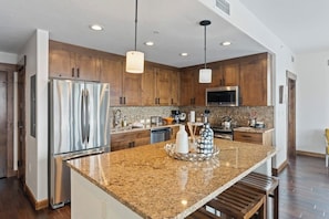 A modern kitchen with wooden cabinets, stainless steel appliances, granite countertops, and pendant lighting. - Luxurious corner condo w/ view & shared pool, hot tubs, game room & more (Steamboat Springs)