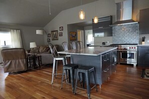 Eine moderne Küche mit einer zentralen Kochinsel, Barhocker und einem Essbereich mit einer Couch und Stühlen.