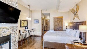 Een hotelkamer met een stenen openhaard, een bed met witte beddengoed, een bureau met een stoel en een aan de muur bevestigde televisie.