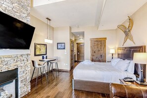 Ein Hotelzimmer mit Kamin aus Stein, einem Bett mit weißer Bettwäsche, einem Schreibtisch mit Stuhl und einem an der Wand montierten Fernseher.