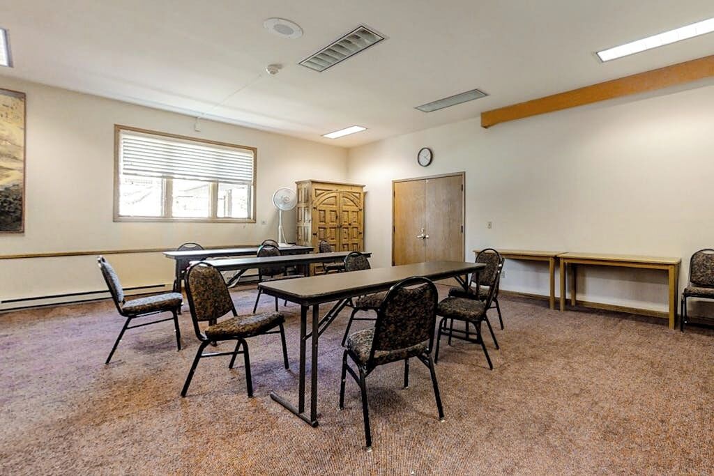 A conference room with a long table, chairs, a clock, a window with blinds, and a door.