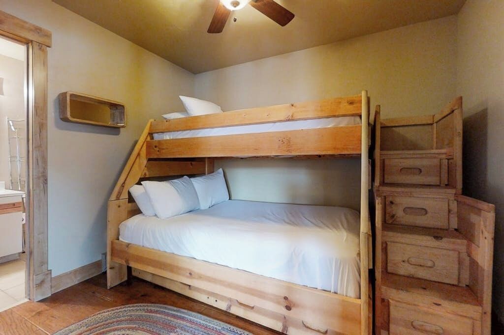 Un lit superposé avec une tête de lit en bois, une petite étagère en bois et un ventilateur de plafond.