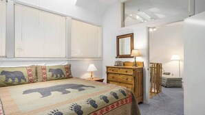 Een slaapkamer met een bed, een dressoir, een spiegel en een raam met jaloezieën.
