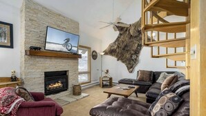Een woonkamer met een stenen openhaard, leren banken, een tv aan de muur en een wanddecoratie van vacht.