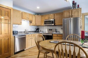A kitchen with wooden cabinets, stainless steel appliances, a dining table with chairs, and a window with red candles. - Loft condo with Flattop Mountain views, shared hot tubs, gas fireplace, & gym (Steamboat Springs)