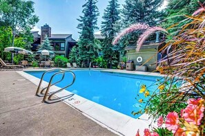 Ein Pool mit Liegestühlen und Sonnenschirmen, umgeben von Bäumen und einem Gebäude im Hintergrund.