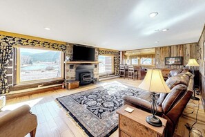 Ein Wohnzimmer mit Kamin, einer Couch, einem Fernseher und einem großen Fenster mit Blick auf eine reizvolle Landschaft.