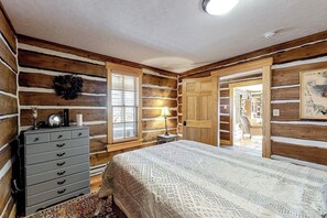 Ein schlafzimmer im Blockhausstil mit Bett, Kommode, Lampe und Blick auf einen Essbereich.