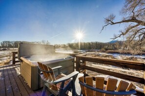 Ein Whirlpool auf einer Holzterrasse mit Stühlen, mit Blick auf eine verschneite Landschaft und einen klaren Himmel.