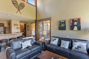 A living room with two sofas, a coffee table, and a kitchen in the background. - Upscale condo with balcony, pool, hot tubs, & fireplace - walk to lifts (Steamboat Springs)