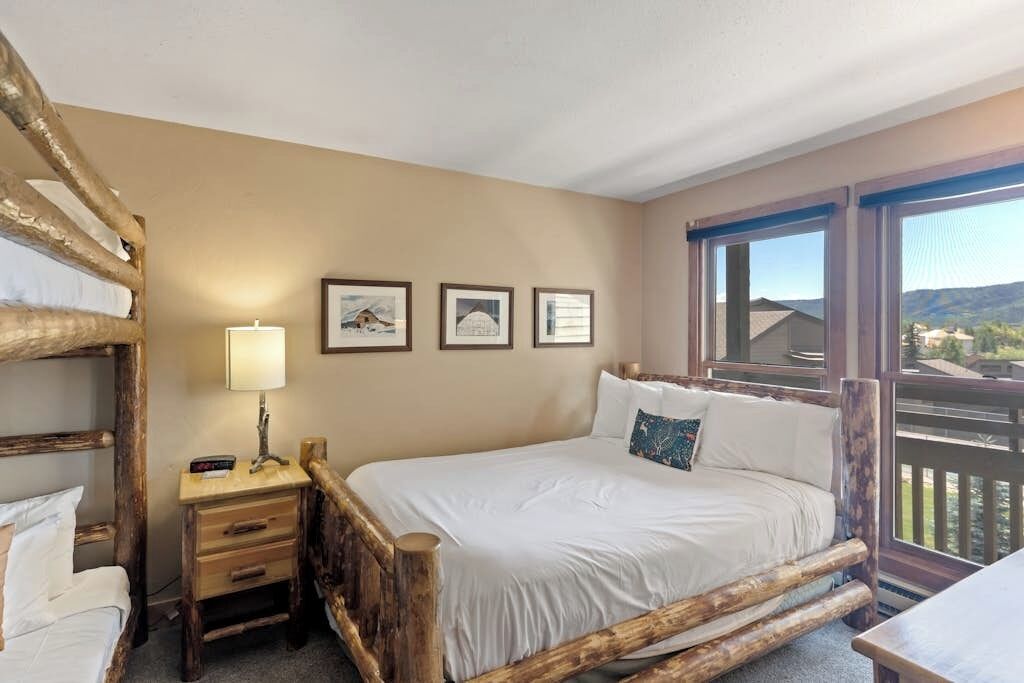 A room with a bunk bed, a bedside table with a lamp, and framed pictures on the wall.