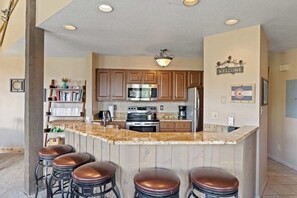 A kitchen with wooden cabinets, a granite countertop, a stainless steel refrigerator, and a bar area with stools. - Upscale condo with balcony, pool, hot tubs, & fireplace - walk to lifts (Steamboat Springs)