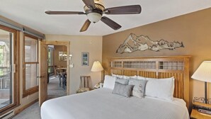 A hotel room with a large bed, a ceiling fan, a mountain artwork on the wall, and a view through the glass door. - The Lodge at Steamboat A301 Upscale condo with balcony, pool, hot tubs, & fireplace - walk to lifts (Steamboat Springs)