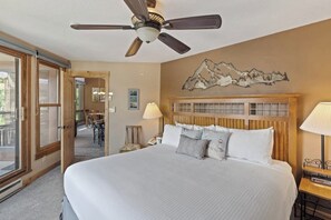A hotel room with a large bed, a ceiling fan, a mountain artwork on the wall, and a view through the glass door. - Upscale condo with balcony, pool, hot tubs, & fireplace - walk to lifts (Steamboat Springs)