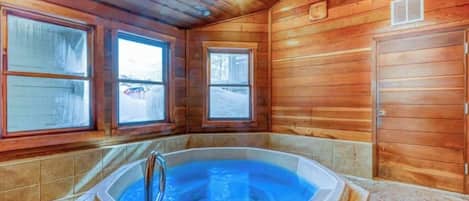 A wooden cabin interior with a hot tub, large windows, and a door.