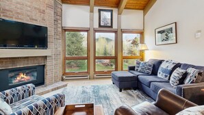 Una sala de estar con chimenea, ventanas amplias, un sofá y un televisor.