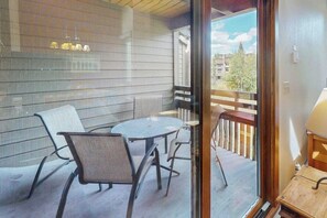 A balcony with a glass door, a round table, two chairs, and a wooden railing. - Updated Steamboat condo with pool, hot tubs, & W/D - near lifts (Steamboat Springs)