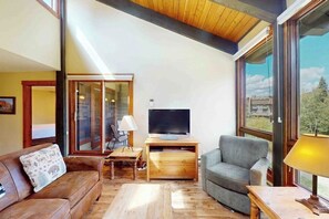 A living room with a wooden ceiling, a television on a wooden stand, a grey sofa, and a wooden coffee table. - Updated Steamboat condo with pool, hot tubs, & W/D - near lifts (Steamboat Springs)