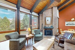 A cozy living room with a fireplace, large windows, and a view of trees. - Updated Steamboat condo with pool, hot tubs, & W/D - near lifts (Steamboat Springs)