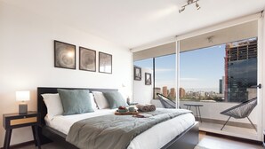 Una camera da letto moderna con un letto grande, un comodino, una sedia e un balcone con vista sulla città.