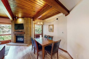 A dining area with a brick fireplace, wooden ceiling, and a dining table with chairs. - Classic Steamboat lodge-style condo with hot tubs & pool (Steamboat Springs)