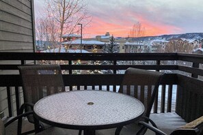 A balcony with a round table and chairs, overlooking a snowy landscape with buildings and a sunset. - Large suite in Steamboat Springs with pool & hot tubs (Steamboat Springs)