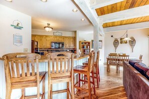 A kitchen with wooden cabinets, a central island with bar stools, and a dining area with a wooden table and chairs. - Perfect Steamboat getaway with hot tubs, pool, washer/dryer & free shuttle (Steamboat Springs)