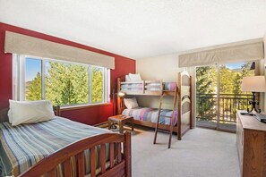 Ein Zimmer mit zwei Betten, einem Schreibtisch und einem Balkon mit Blick auf Bäume.