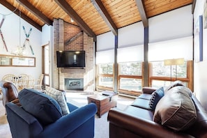 Ein Wohnzimmer mit Kamin, Holzbalkendecke, Fernseher und großen Fenstern.