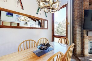 Ein Essbereich mit Holztisch, Stühlen, einer Chandelüster und einem Kamin aus Backstein.