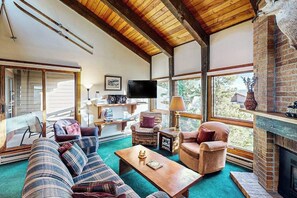 Ein gemütliches Wohnzimmer mit Kamin, bequemen Sitzgelegenheiten und großen Fenstern.